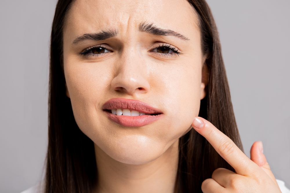 Close-up of a woman touching her right cheek with a puzzled or worried expression.