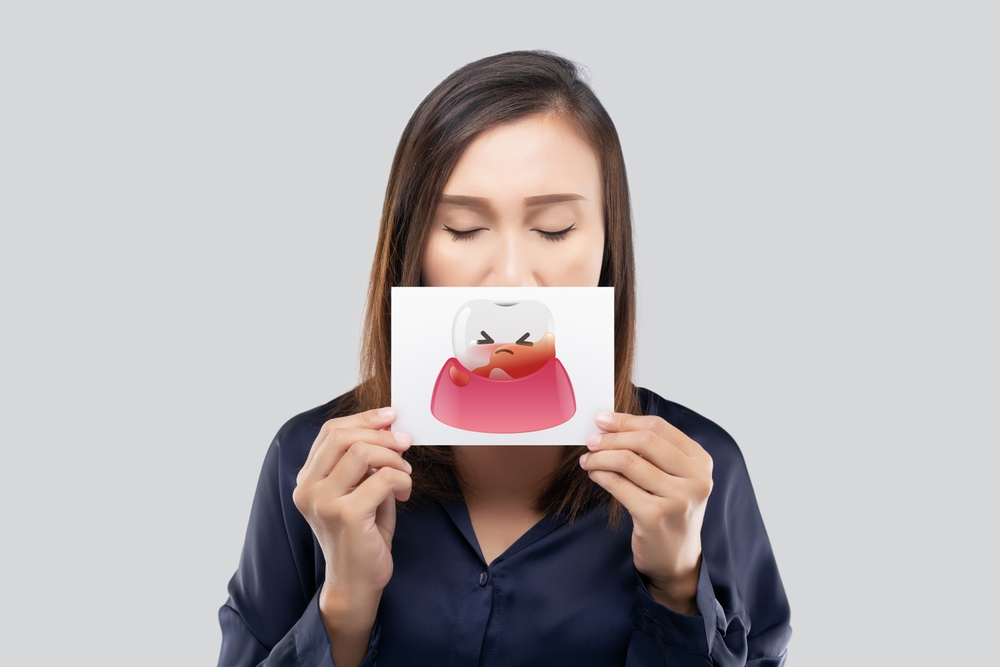 Woman holding a card with a cartoon mouth illustration in front of her face, eyes closed, neutral background